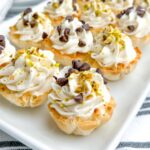 mini cannoli topped with chocolate chips and pistachios on a white platter.