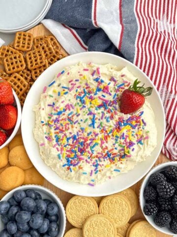 sugar cookie dip in a white bowl with pretzels, fruit, and cookies.