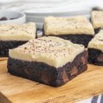 brownie with cream cheese frosting on a wooden cutting board.