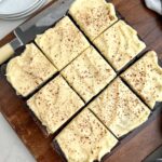 brownies with cream cheese frosting on a wooden cutting board.