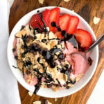 strawberry banana smoothie bowl with toppings in a white bowl on a wooden board.