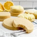 a lemon cut out cookie with a bite taken out stacked on another cookie on a blue and white towel on a wooden cutting board.