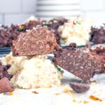 stack of white, milk, and dark chocolate coconut clusters cut in half on parchment paper.