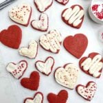 heart shaped red velvet cut out cookies with cream cheese frosting on a white countertop.
