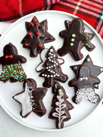 chocolate cut out cookies with chocolate cookie icing that hardens on a white plate.