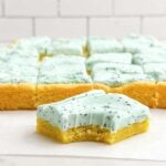 lemon bar with poppy seed cream cheese frosting on a white countertop.