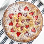 baked strawberry ricotta cake topped with powdered sugar on a white plate.