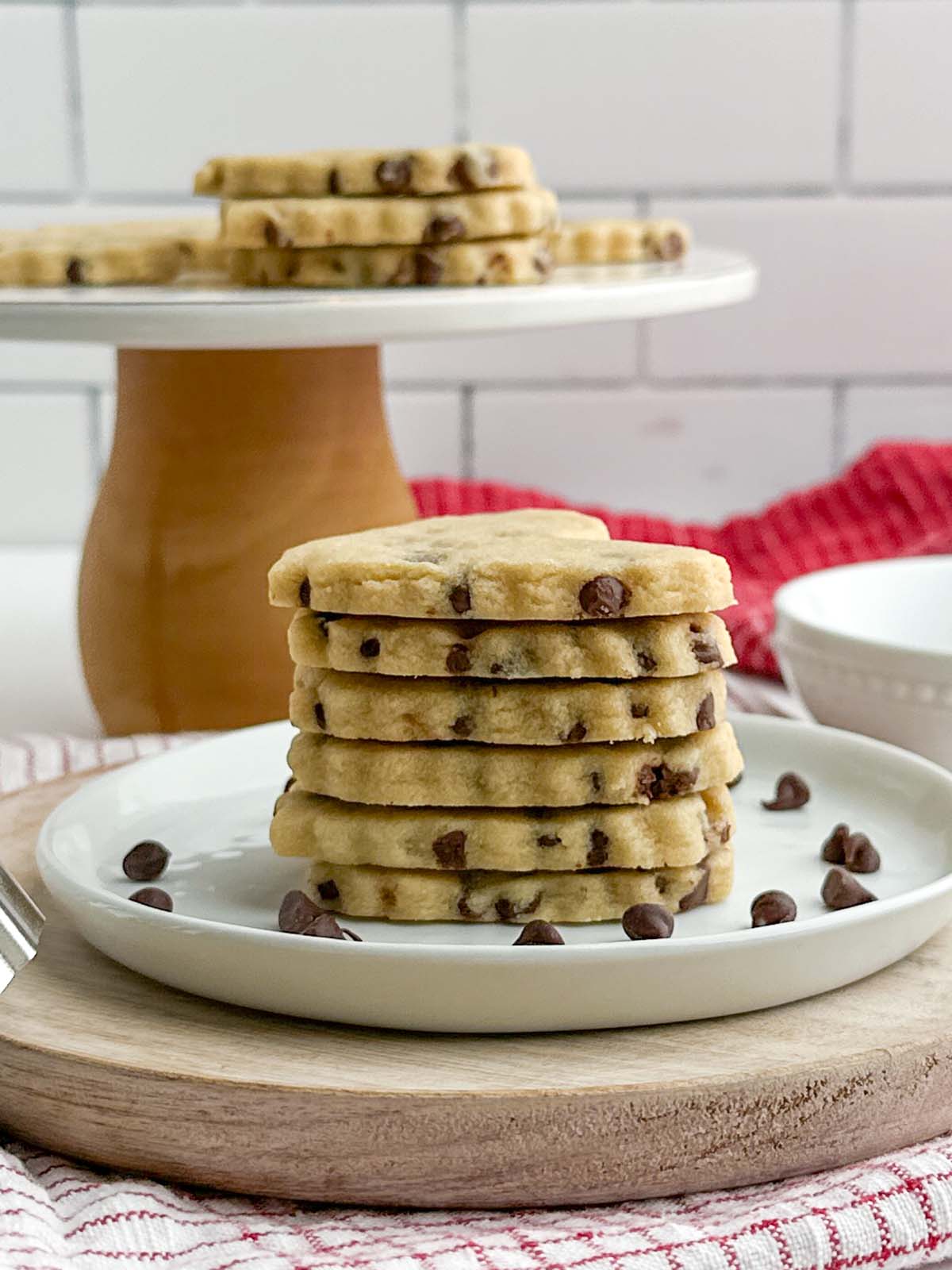 side view of stack of chocolate chip cutout cookies on a white plate.