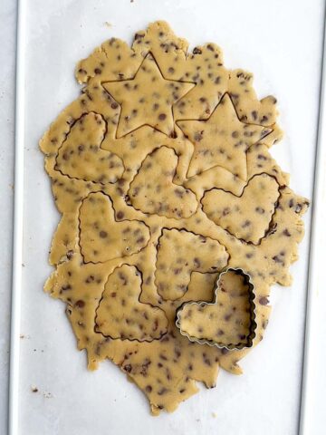 rolled out chocolate chip cutout cookie dough with cutouts in the dough and a cookie cutter on top.