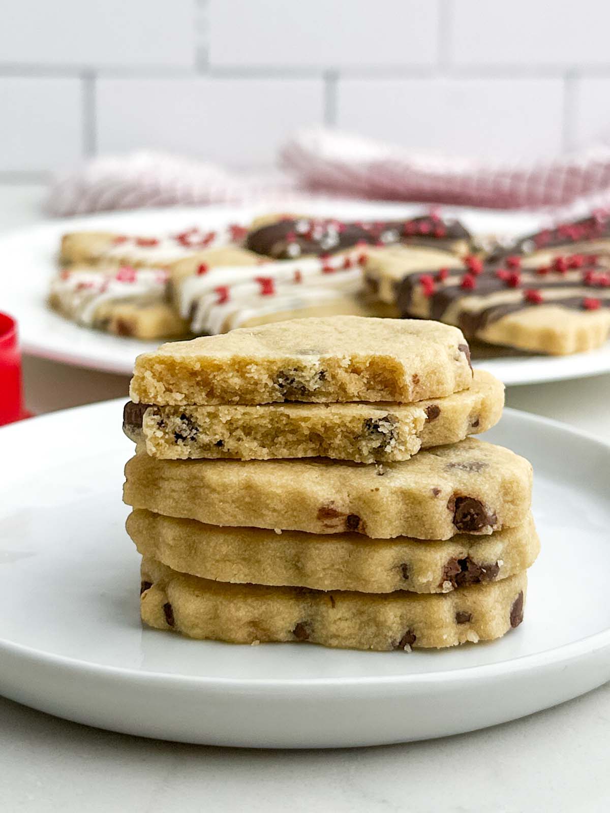 side view of stack of chocolate chip cutout cookies on a white plate.