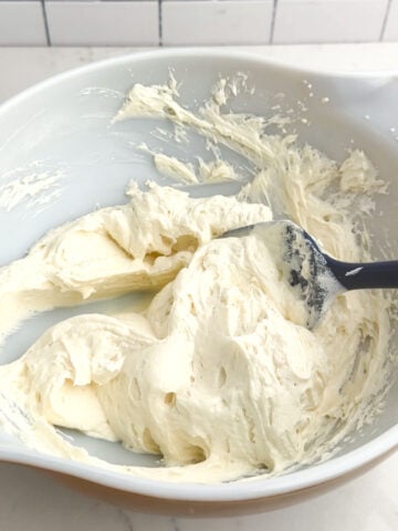 spatula folding cool whip into cream cheese mixture in a white mixing bowl.