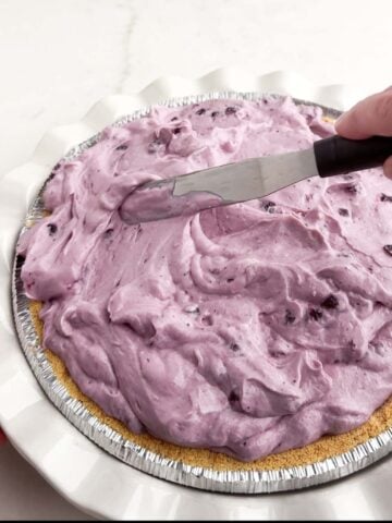 offset spatula spreading blueberry cream cheese pie filling into a graham cracker crust.