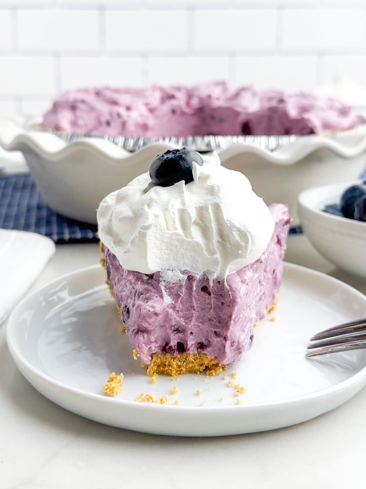 front view of a piece of blueberry cream pie with a bite removed.