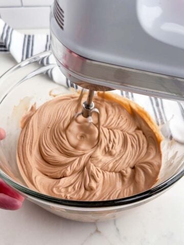 mixer beating chocolate whipped cream in a clear bowl.