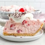 side view of a slice of no bake cherry pie topped with whipped cream, chocolate shavings, and a cherry.
