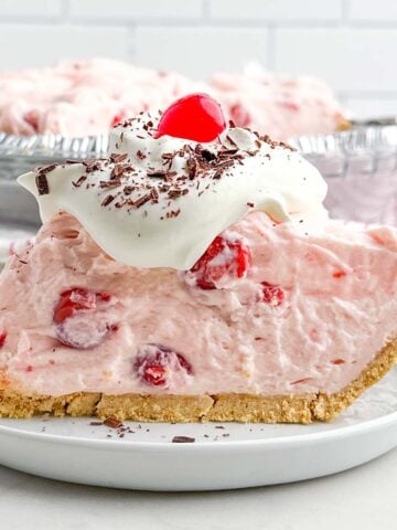 side view of a slice of no bake cherry pie topped with whipped cream, chocolate shavings, and a cherry.