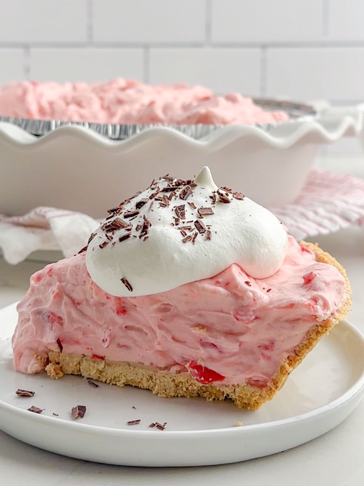 side view of a slice of no bake cherry pie topped with whipped cream and chocolate shavings.