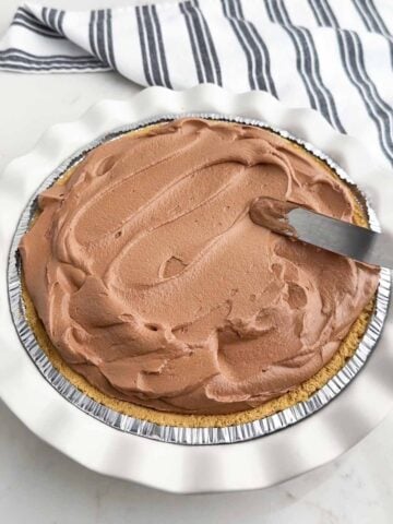 spatula spreading chocolate mousse into a graham cracker crust.