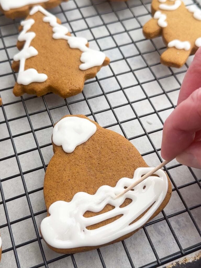 hand holding a toothpick spreading icing onto a gingerbread cookie.