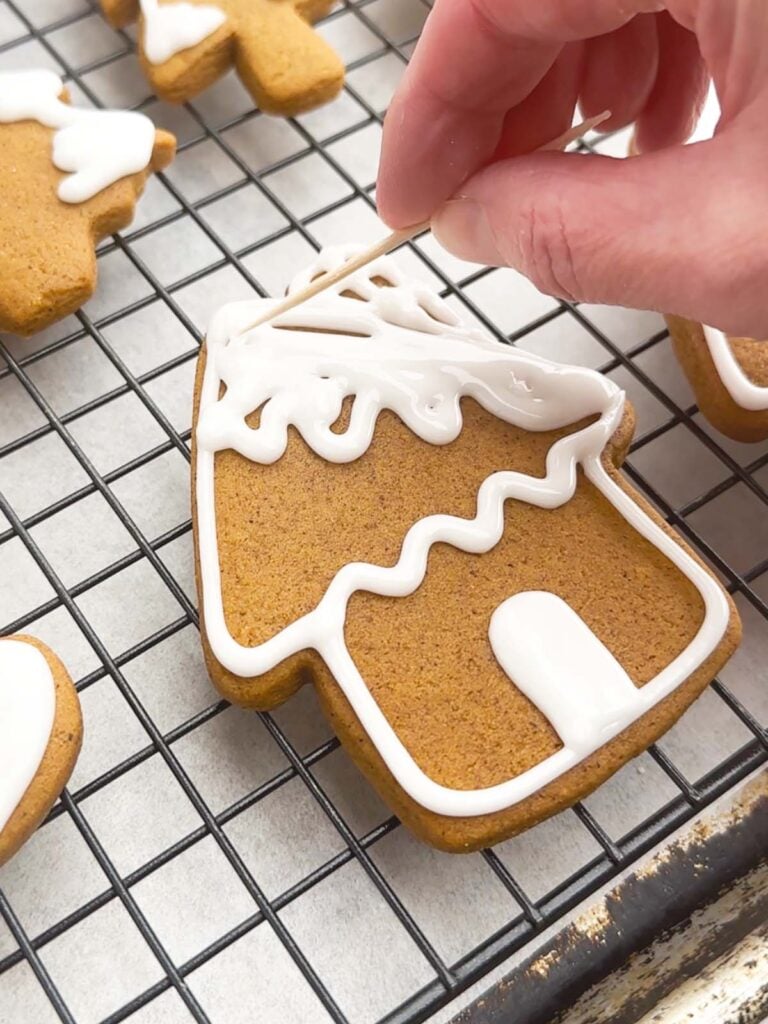 hand holding a toothpick spreading icing onto a gingerbread cookie.