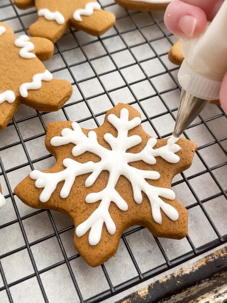 hand piping icing onto a gingerbread cookie.