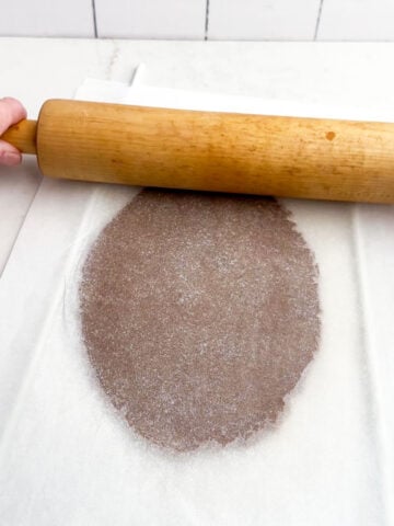 gingerbread cookie dough rolled out between layers of parchment paper.