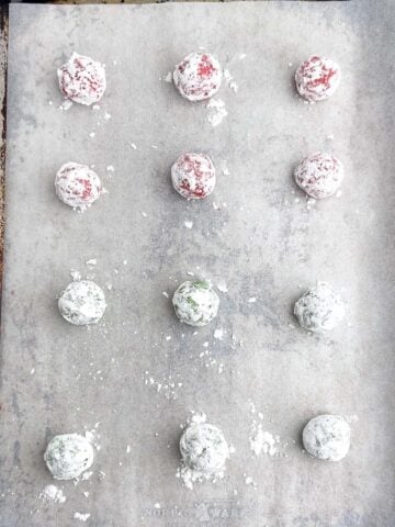 cookie dough balls rolled in powdered sugar on a baking sheet.