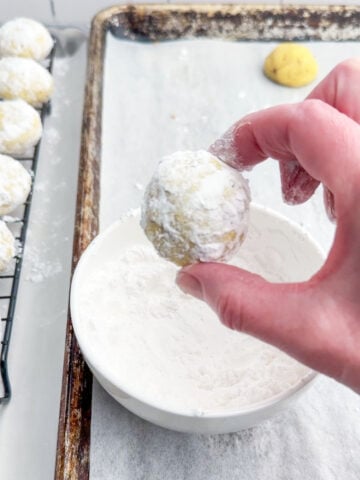 hand holding up a lemon snowball cookie rolled in powdered sugar.
