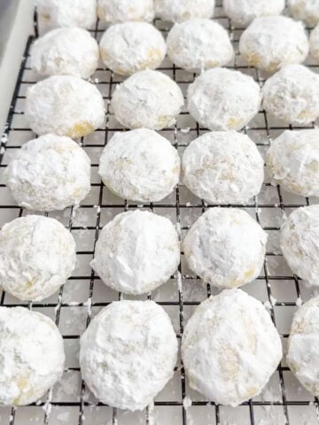 lemon snowball cookies rolled in powdered sugar on a baking rack.